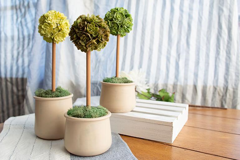 A trio of Oui by Yoplait yogurt jars painted and filled with small topiary trees.