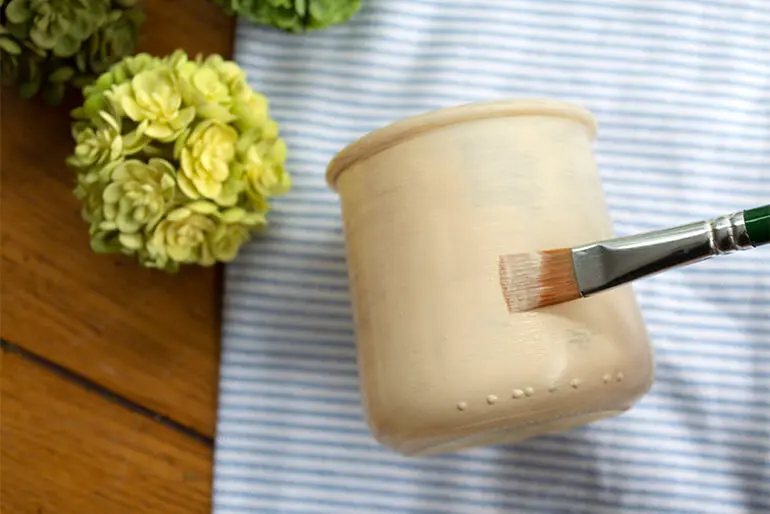 Paint brush with brown craft paint painting a Oui by Yoplait yogurt jar.