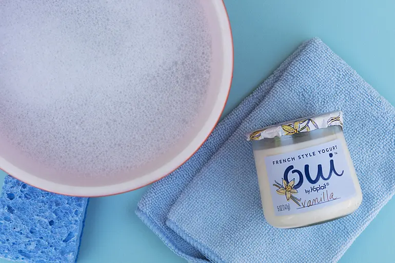 A bowl of soapy water with a jar of Oui by Yoplait yogurt next to it on a towel.