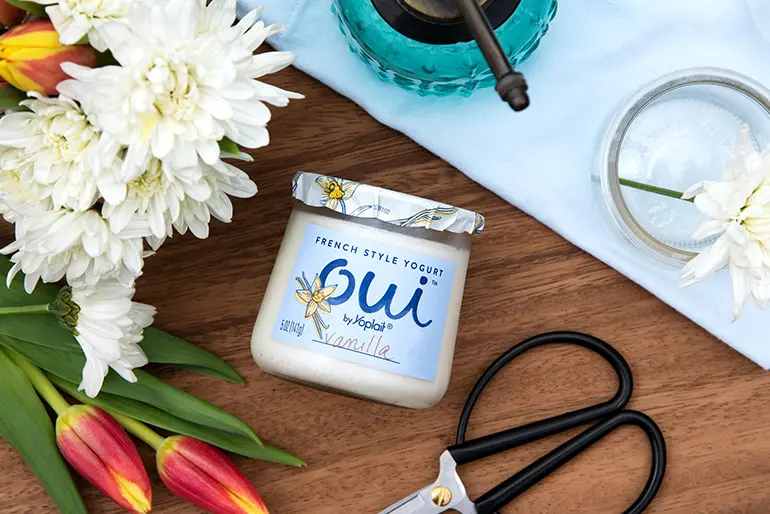 A Oui by Yoplait yogurt jar with flowers next to it as well as scissors and a spray bottle.
