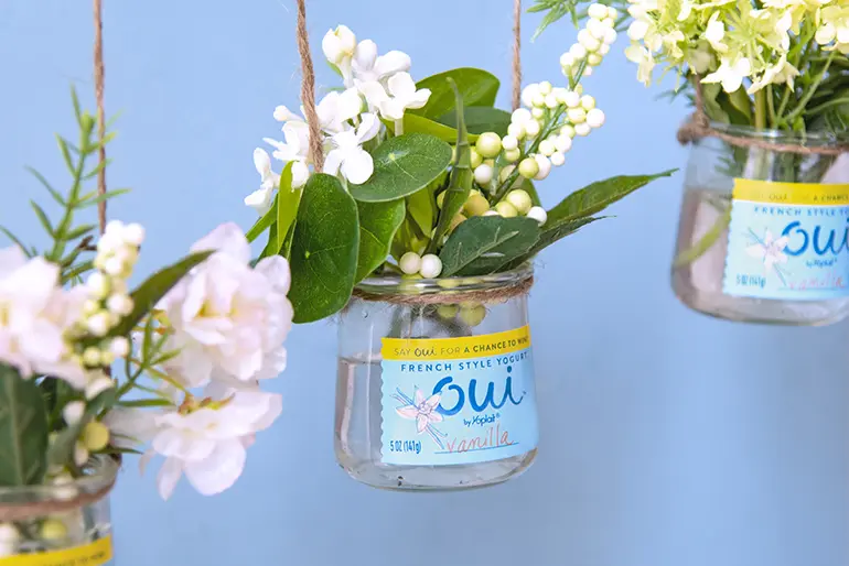 Three Oui by Yoplait yogurt jars used as holders for flowers as they suspend from the ceiling.