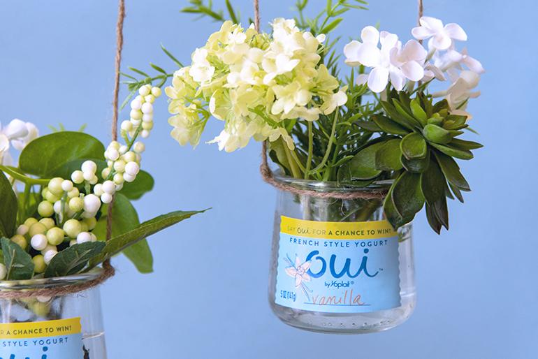 A Oui by Yoplait yogurt glass jar hanging, with a bouquet of flowers in it.