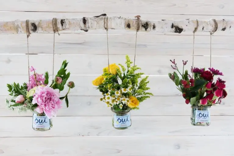 Three bouquets of flowers hanging from a log in Oui by Yoplait yogurt jars.