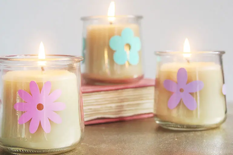 Three flower art decorated Oui by Yoplait yogurt jars housing lit candles next to a book.