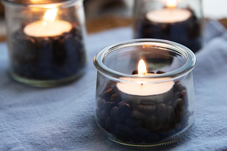 A tealight candle holder made from a Oui glass jar, half filled with brown stones.