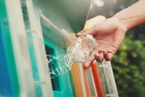 A hand putting an empty plastic bottle into a blue recycling bin.